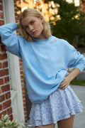 Light blue crewneck sweatshirt with small floral chest graphic, worn by model