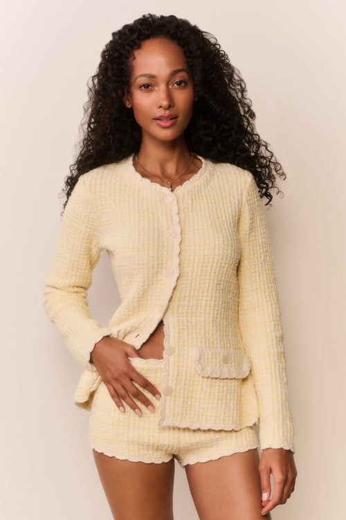 Woman wearing a light yellow textured cardigan and shorts set against a plain background