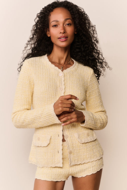 Woman wearing a light yellow textured cardigan and shorts set against a plain background