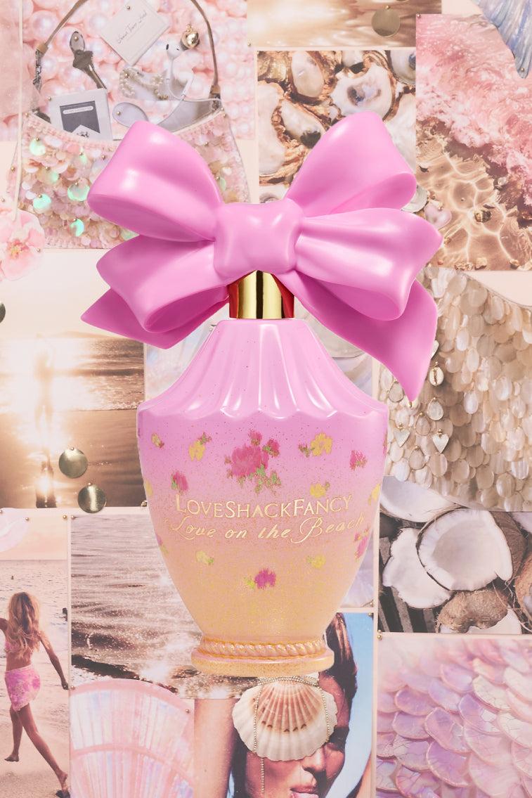 Pink Love on the Beach eau de parfum bottle with bow surrounded by beach-themed props