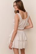 White eyelet crop top with lace-trimmed scoop back and sleeveless ruffles, button front