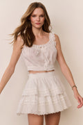 White sleeveless eyelet crop top with ruffled hem, lace-trim neckline, and button front
