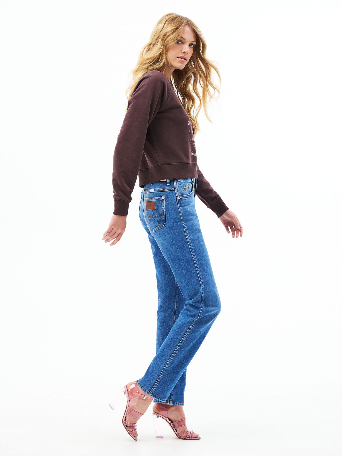 Medium wash cowboy cut jeans on model with flared leg and stitched front pockets