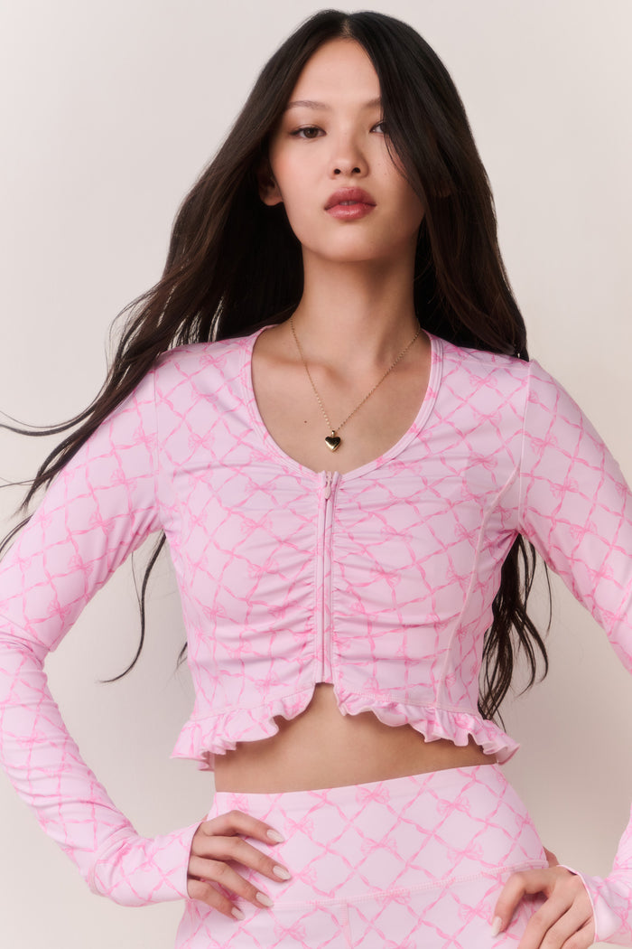 Pink printed zip-up active top with long sleeves, front zipper, and ruffled crop hem