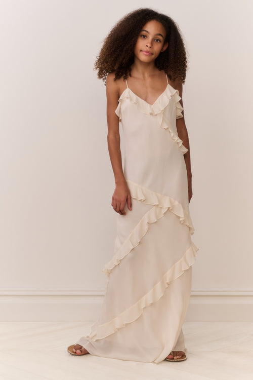 Tween girl wearing a flowing white sleeveless dress with ruffles on a plain background