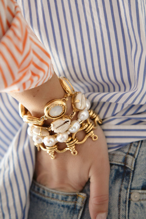 Gold link bracelet on wrist with white bead and shell accents