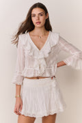 White pleated mini skirt with lace trim and layered ruffle hem, front view
