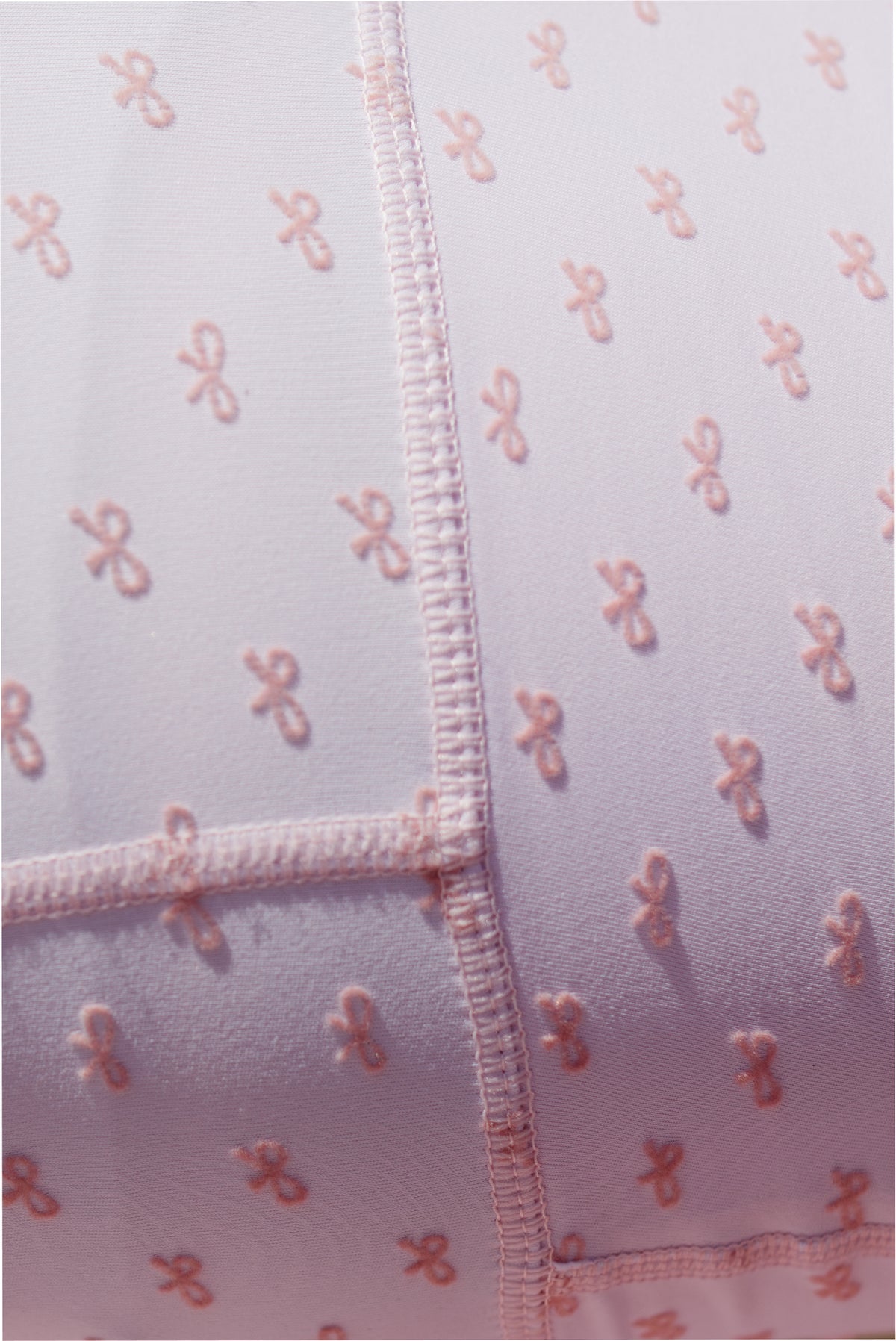 Close-up of mauve-pink bow-print fabric with stitched trim and zip placket