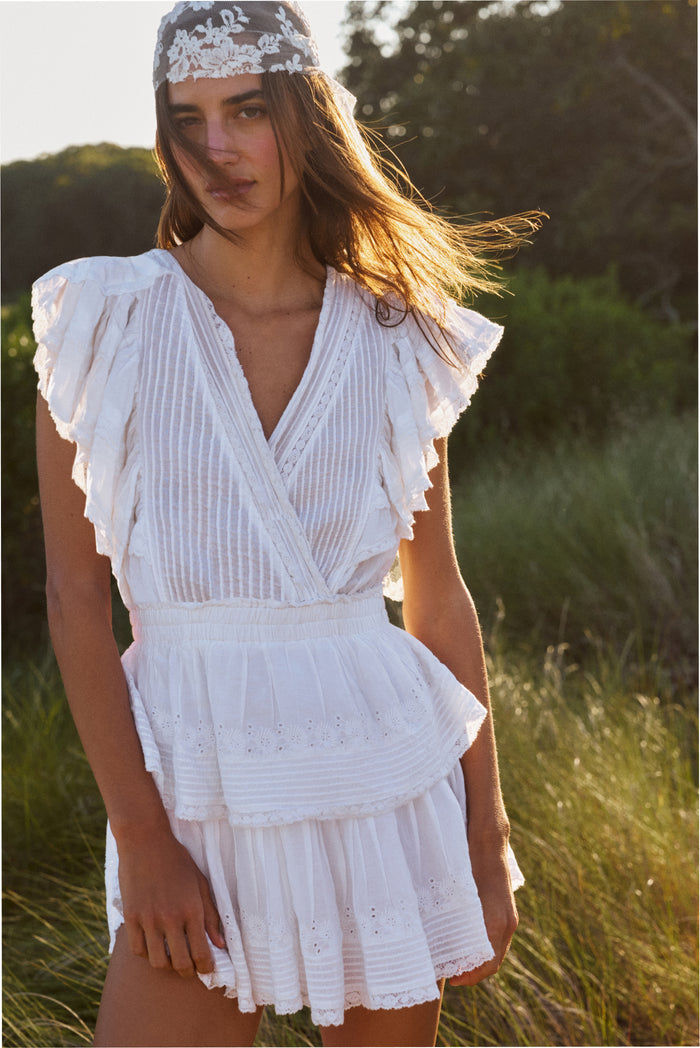 White mini dress with V-neck, ruffled cap sleeves, tiered skirt; wears floral headband
