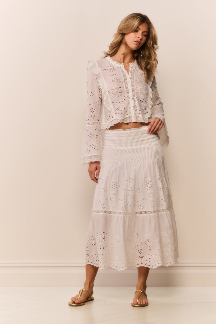 Woman wearing a white lace eyelet maxi skirt and matching long sleeve blouse against a plain background