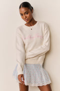 Cream cotton pullover front view with pink embroidered script and ribbed cuffs