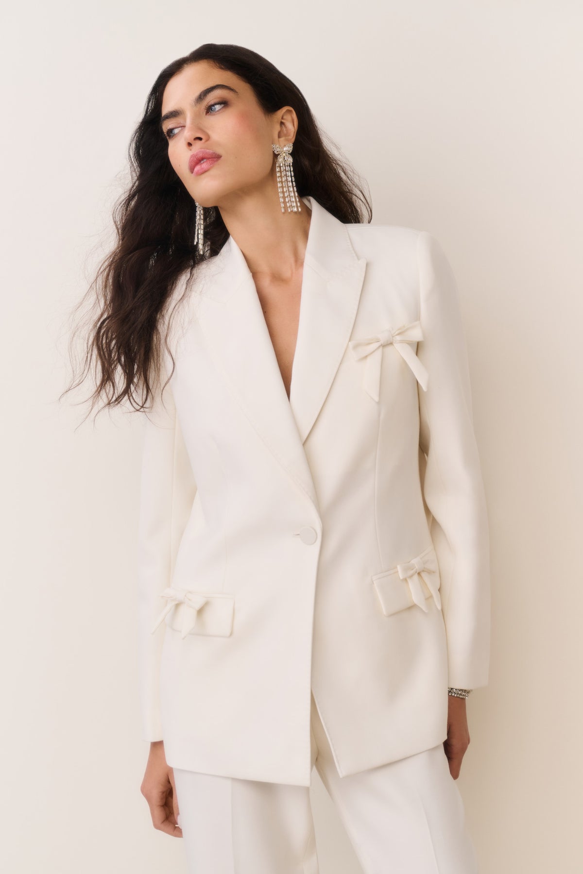 Cream wool-blend blazer with bow embellishments on lapel, cuffs, and flap pockets, close-up
