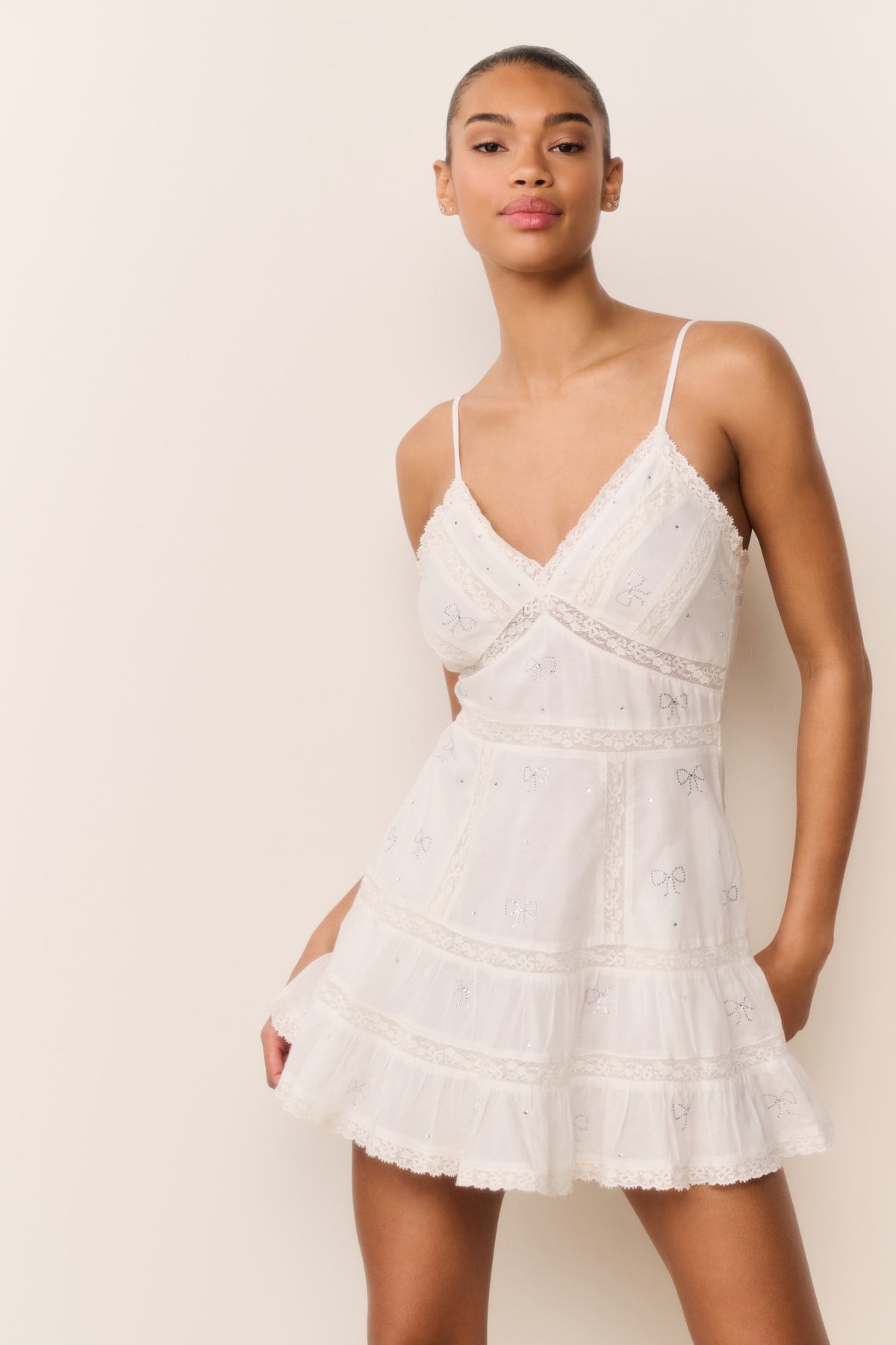 White cotton mini dress with V-neck and spaghetti straps, tiered ruffles and bow print