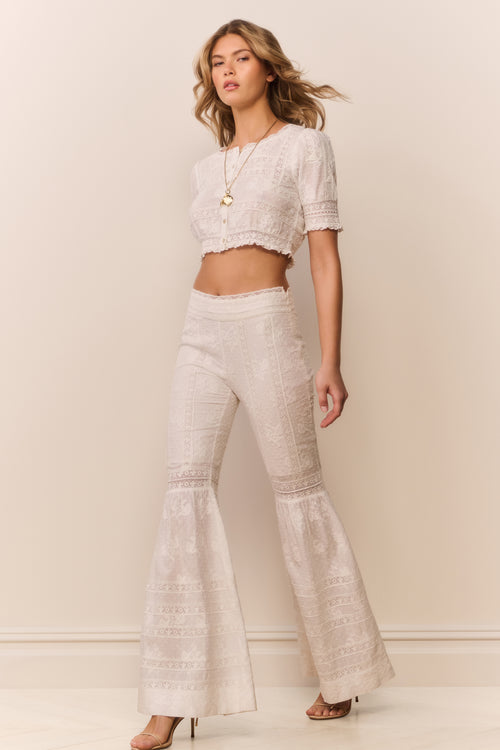White cotton bell-bottom pants, front three-quarter view with embroidered panels and flare