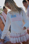 Ivory long-sleeve flag pullover worn with ruffled skirt, outdoor scene