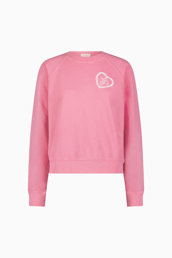 Pink crewneck sweatshirt flat lay with small heart-and-bow logo on chest