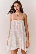 White Victorian mini dress with thin straps, lace overlay, and tiered skirt
