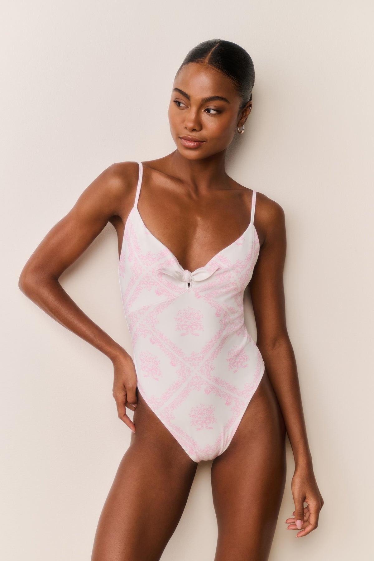 Ivory one-piece swimsuit with pink toile print, sweetheart neckline, thin straps, bust bow