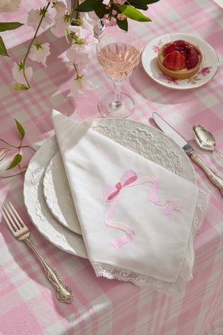 White embroidered napkin with pink bow-like motif and lace-trim border