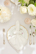 White cloth napkin heart fold with lace edging and small floral embroidery